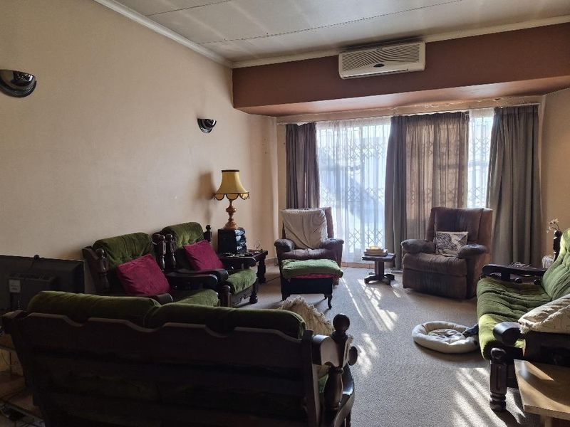 A spacious living room featuring wall-mounted air conditioning, wall sconces, and large windows with curtain tracks, offering a functional layout for relaxation.