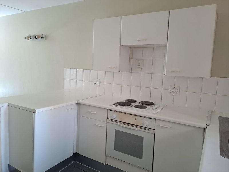 A compact kitchen featuring white built-in cabinetry, a tiled backsplash, and a built-in electric oven and hob.