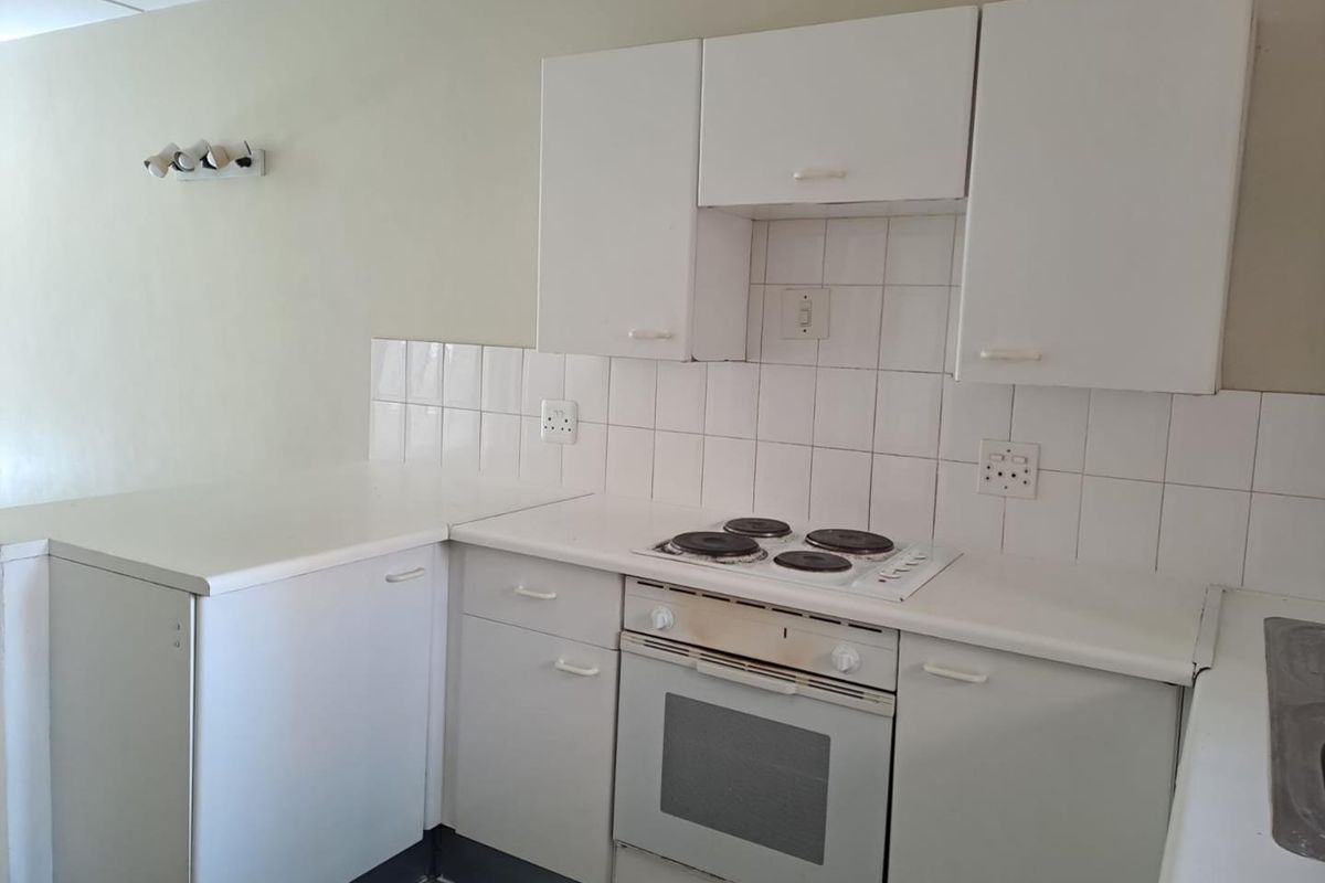A compact kitchen featuring white built-in cabinetry, a tiled backsplash, and a built-in electric oven and hob.