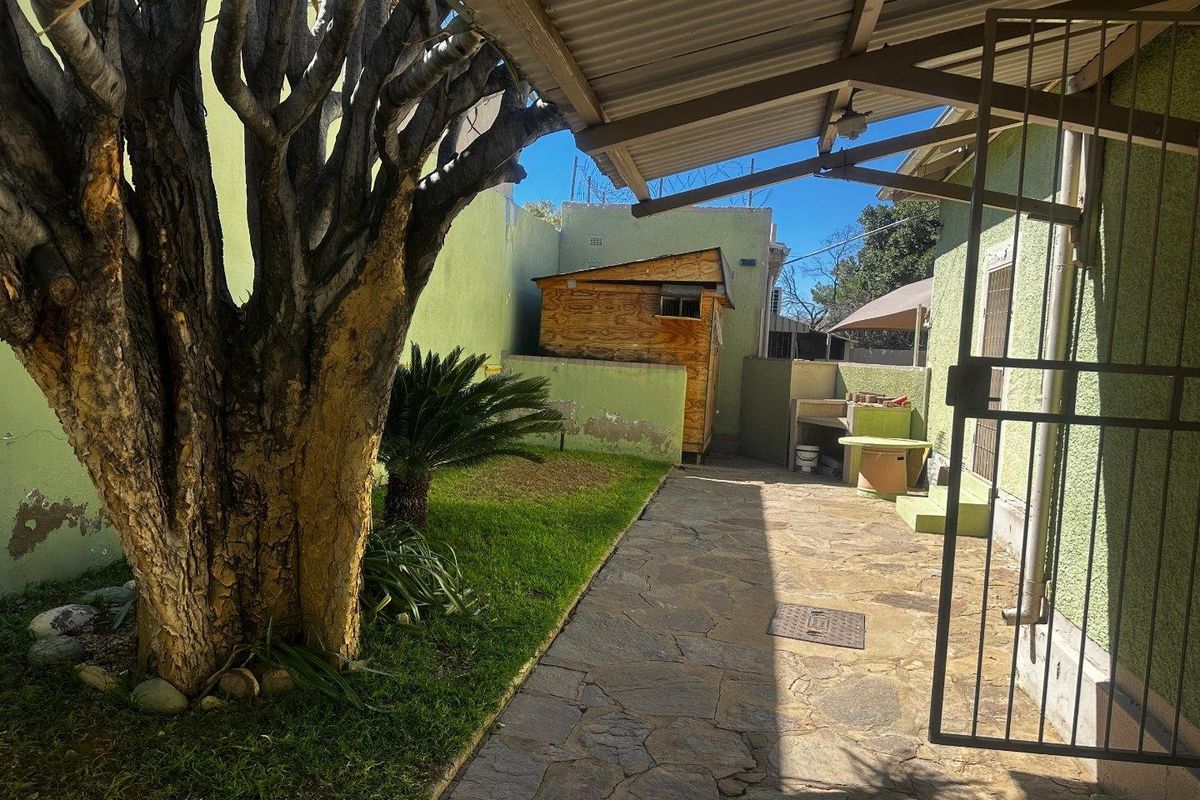 Rear courtyard area featuring stone paving, a covered patio section with a built-in braai, and a small garden space with boundary walling.