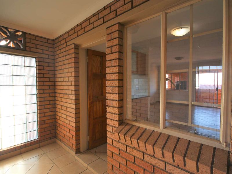 A bright hallway featuring face brick walls, tiled flooring, and a unique glass block window, providing a view into the adjacent living area.