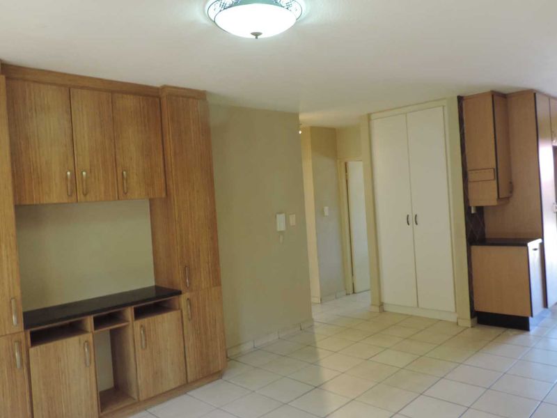 An empty kitchen area featuring built-in wooden cabinetry, tiled flooring, and ample storage space, presenting a functional layout ready for updates.