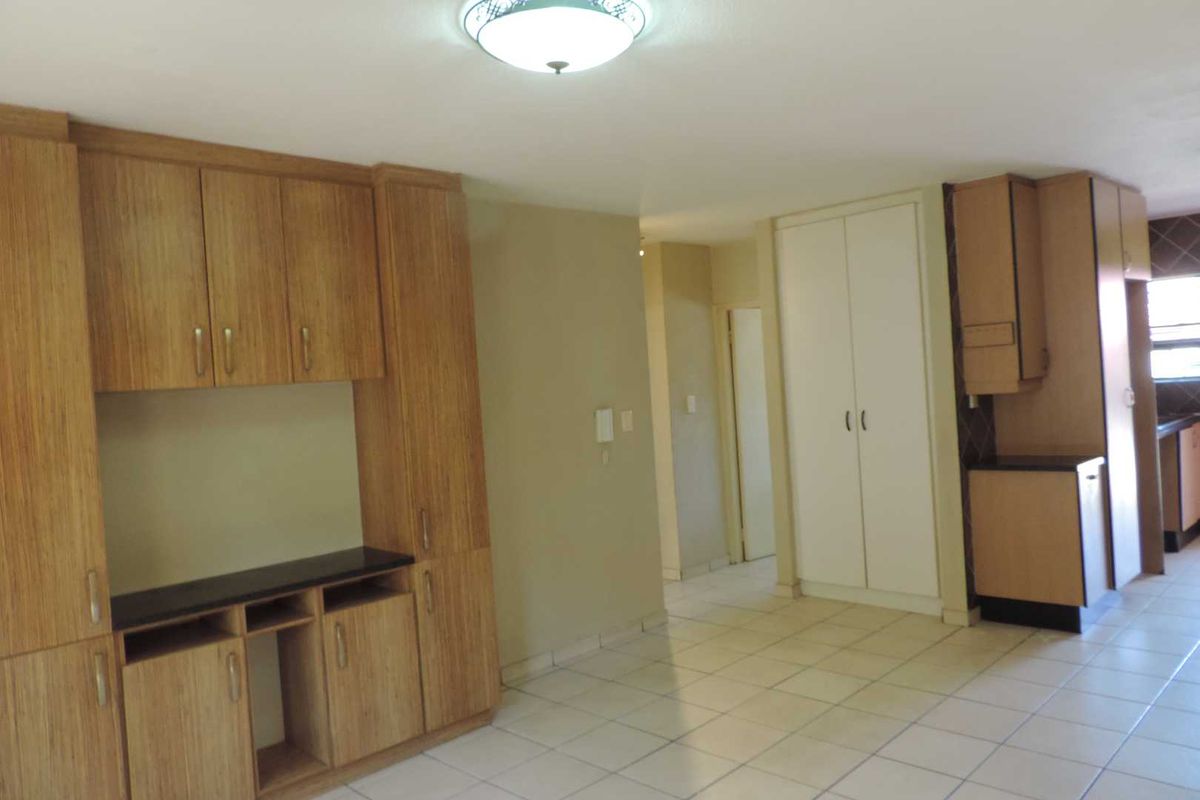 An empty kitchen area featuring built-in wooden cabinetry, tiled flooring, and ample storage space, presenting a functional layout ready for updates.