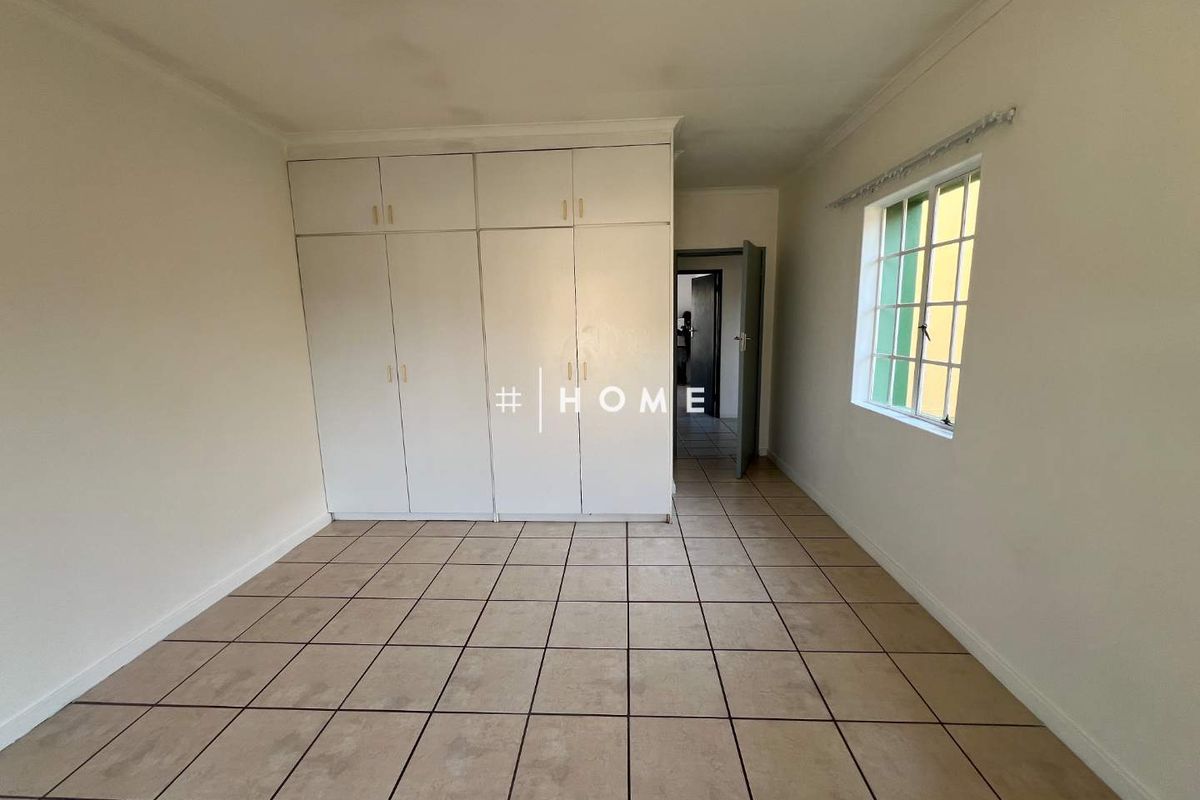 An empty bedroom featuring built-in cupboards, tiled flooring, and a window with security bars.