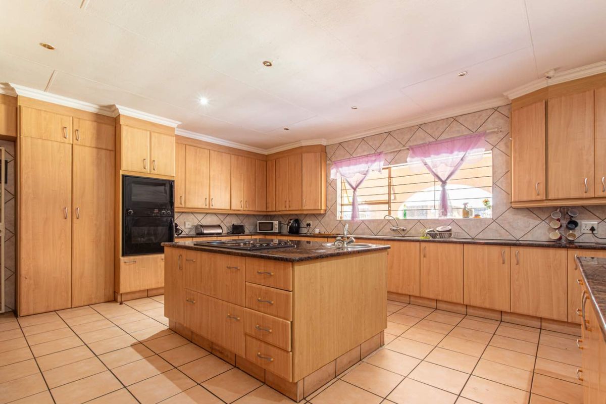 Spacious kitchen featuring light wood cabinetry, a central island with a built-in hob, granite countertops, and tiled flooring throughout.