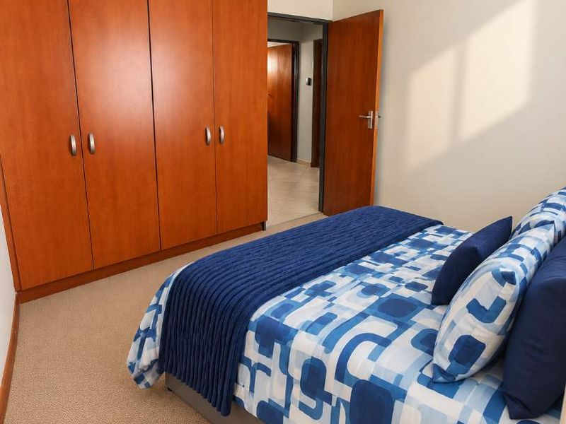 A well-maintained bedroom featuring built-in wooden cupboards, a ceiling fan, and neutral carpeting, offering a functional and comfortable living space.