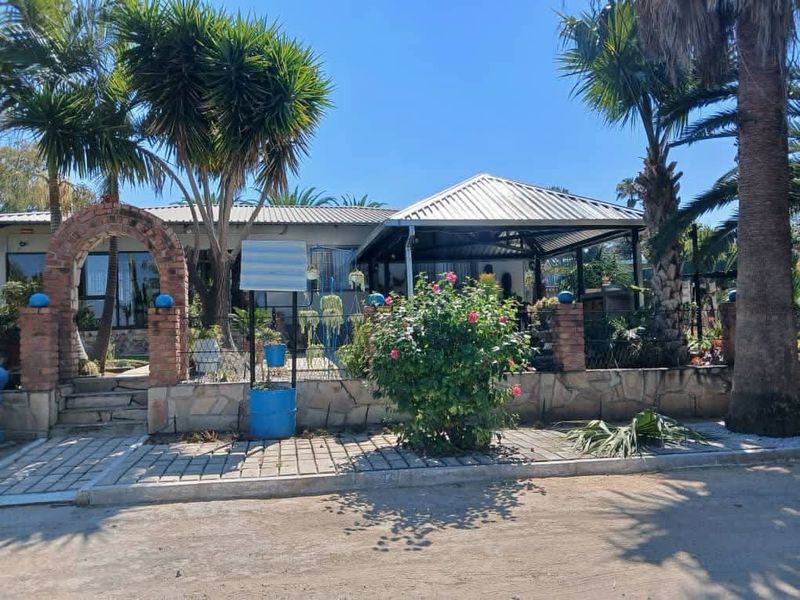 Front exterior view of the property featuring a brick archway entrance, stone retaining wall, and a covered patio area with mature palm trees.