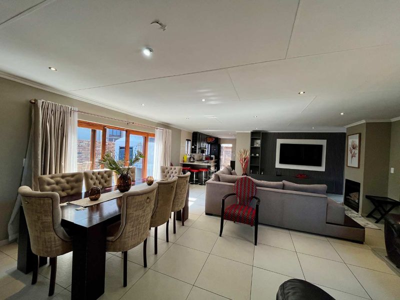 Spacious open-plan living and dining area featuring tiled floors, a modern fireplace, slatted feature wall, and large sliding doors leading to the patio.