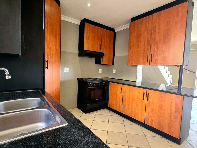 A functional kitchen featuring wood-tone cabinetry, black granite countertops, a double sink, and a built-in oven with an extractor fan.