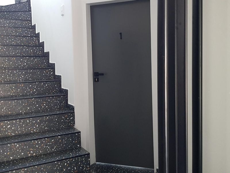 A modern hallway featuring a sleek terrazzo staircase and a dark grey entrance door with minimalist hardware.