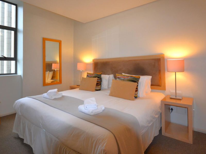 A well-maintained bedroom featuring neutral wall tones, carpeted flooring, and a large window providing natural light.
