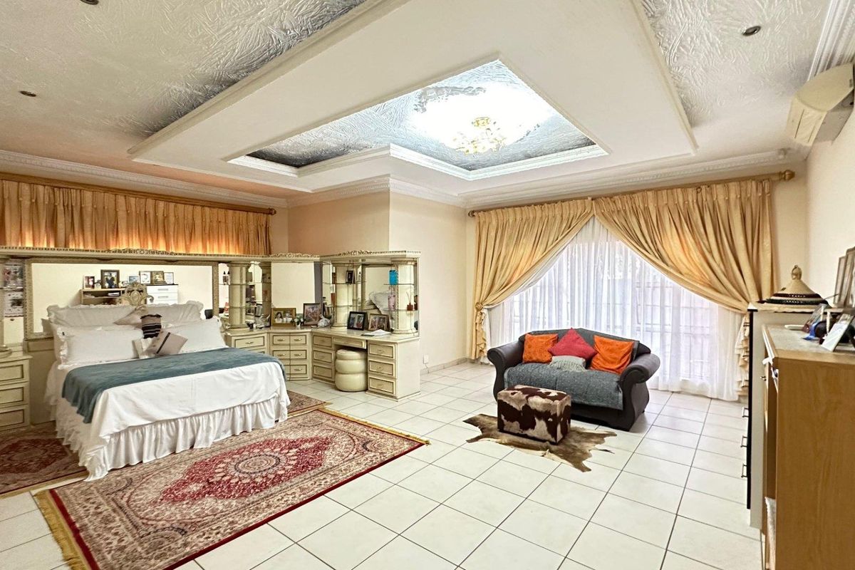Spacious bedroom featuring a recessed tray ceiling with decorative detail, tiled flooring, and large sliding glass doors leading to the exterior.