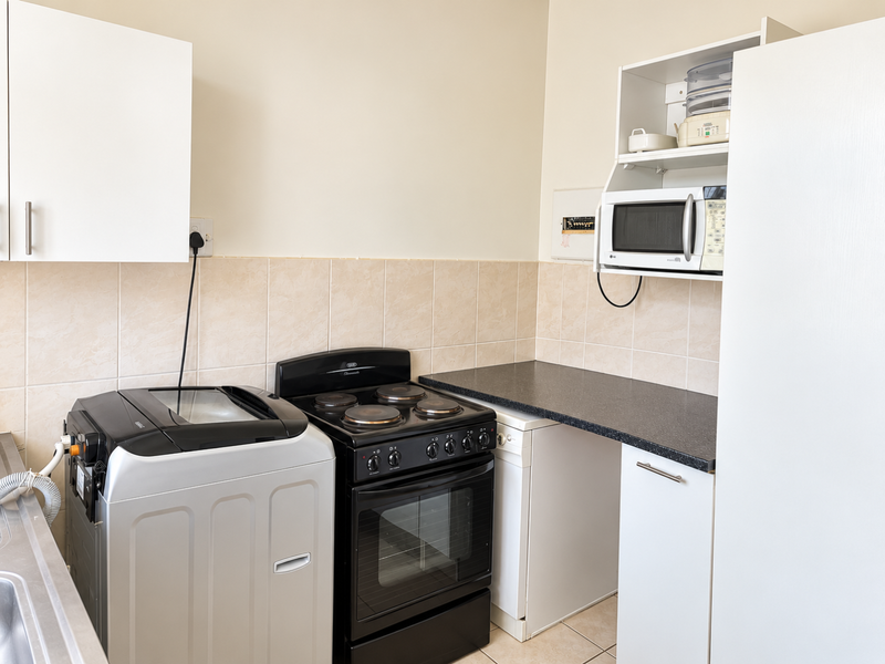 A functional kitchen area featuring white cabinetry, dark countertops, a ceramic tile backsplash, and a built-in electric stove with an integrated microwave shelf.