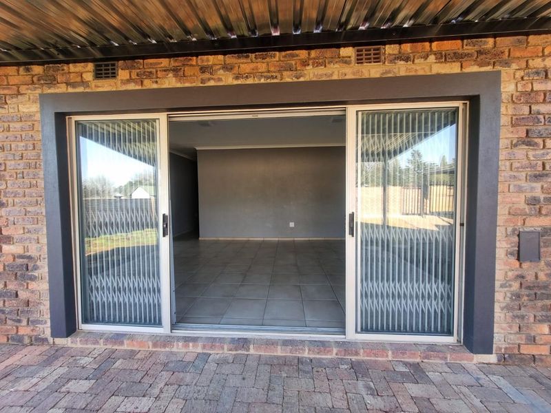 A covered patio area featuring brick masonry, tiled flooring, and large sliding glass doors leading into an open-plan interior space.