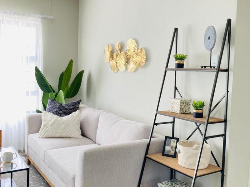 A bright and well-maintained living room featuring neutral wall tones, tiled flooring, and natural light from a window with a curtain rod.