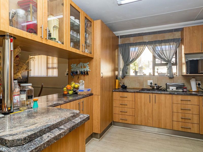 Functional kitchen featuring wood-look laminate cabinetry, granite countertops, a breakfast bar, and a tiled backsplash with a built-in hob.