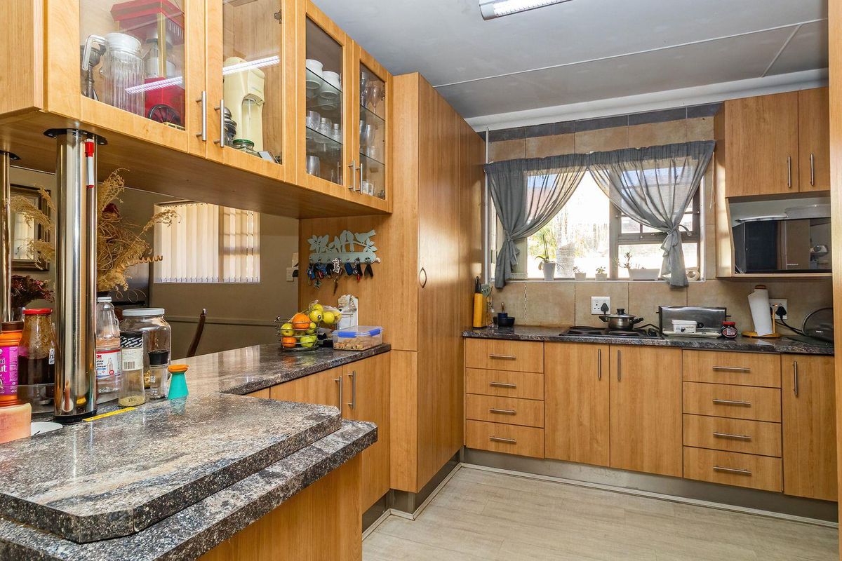 Functional kitchen featuring wood-look laminate cabinetry, granite countertops, a breakfast bar, and a tiled backsplash with a built-in hob.