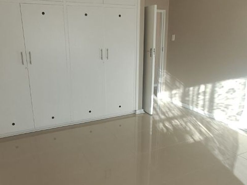 A bright, empty bedroom featuring neutral tiled flooring and extensive white built-in cupboards, offering a clean and versatile living space.