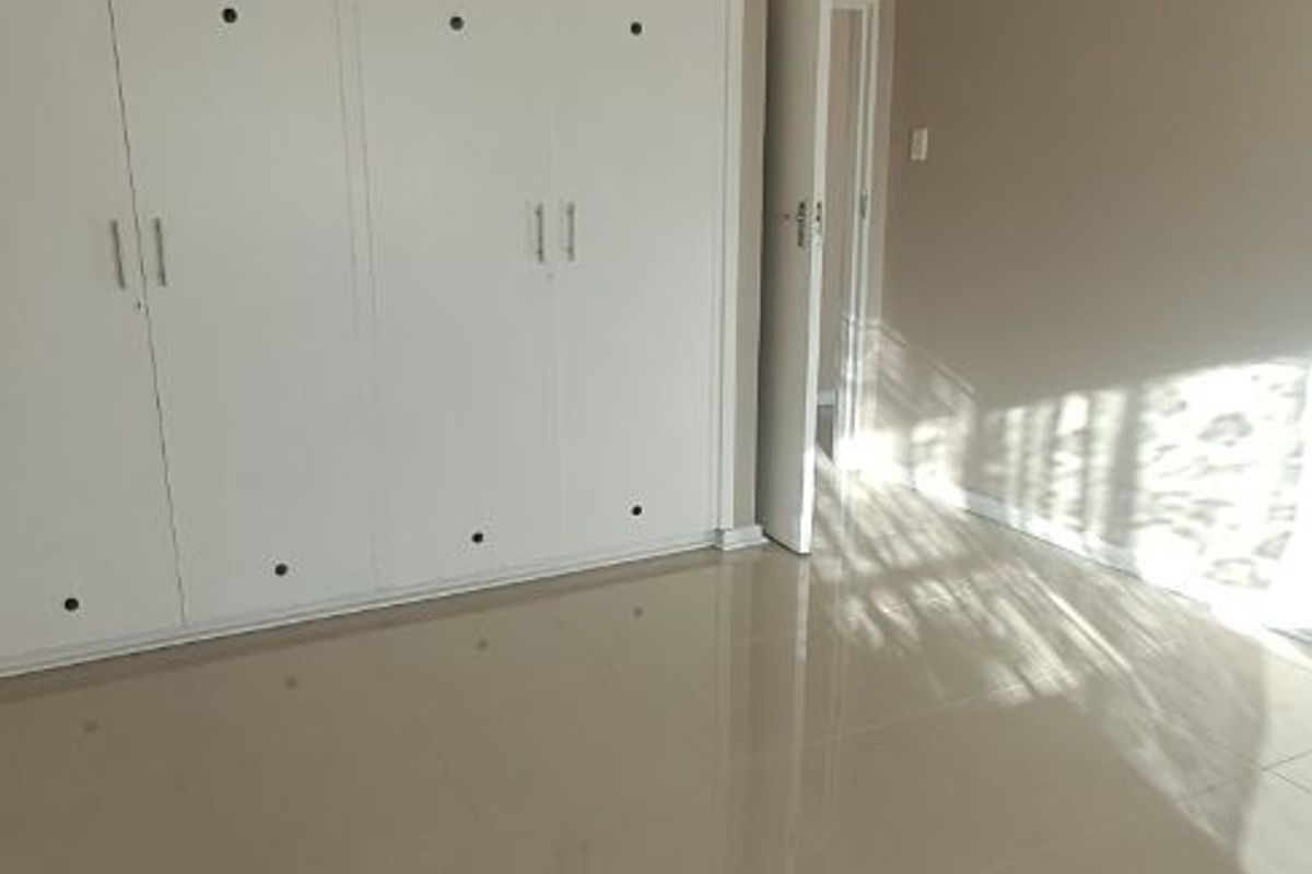 A bright, empty bedroom featuring neutral tiled flooring and extensive white built-in cupboards, offering a clean and versatile living space.