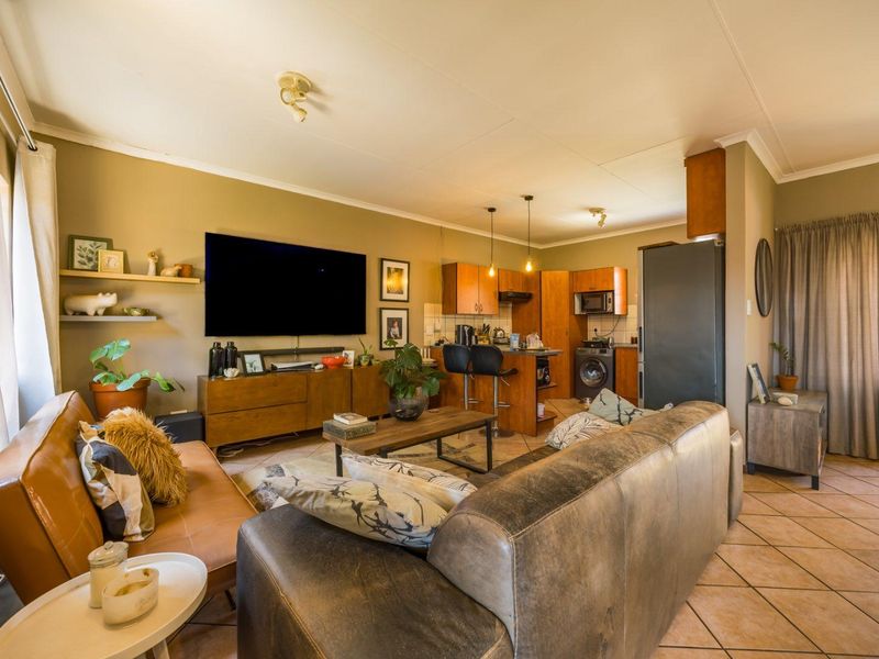 Open-plan living area featuring a functional kitchen with built-in cabinetry and tiled flooring, seamlessly flowing into a comfortable lounge space.