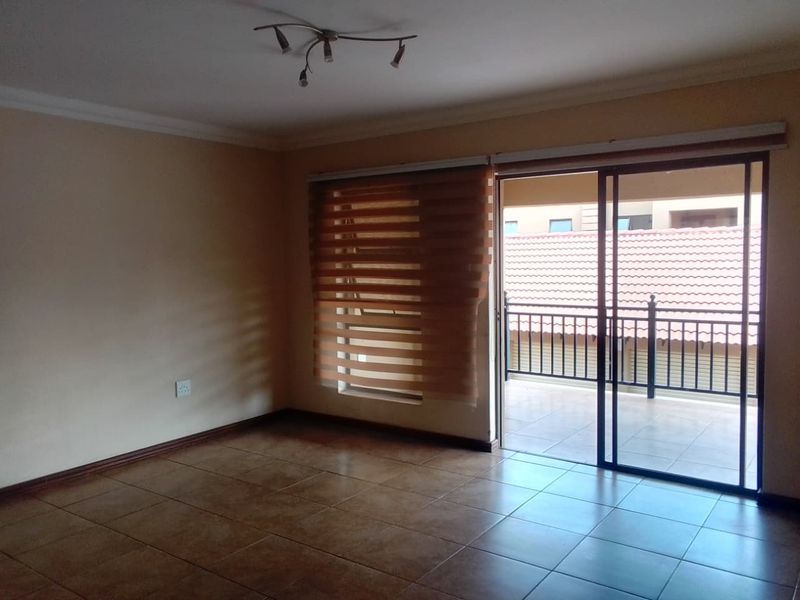 An empty living room featuring tiled flooring, a ceiling light fixture, and a sliding glass door providing access to a balcony.