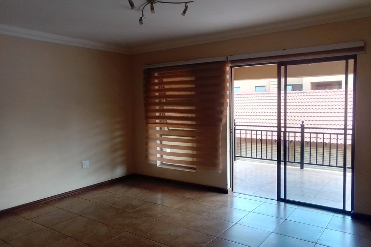 An empty living room featuring tiled flooring, a ceiling light fixture, and a sliding glass door providing access to a balcony.