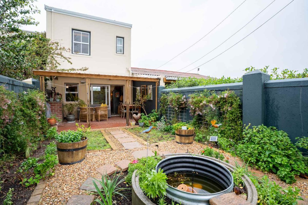 Rear garden area featuring a covered timber patio, brick paving, gravel landscaping, and a built-in metal water feature against a private boundary wall.