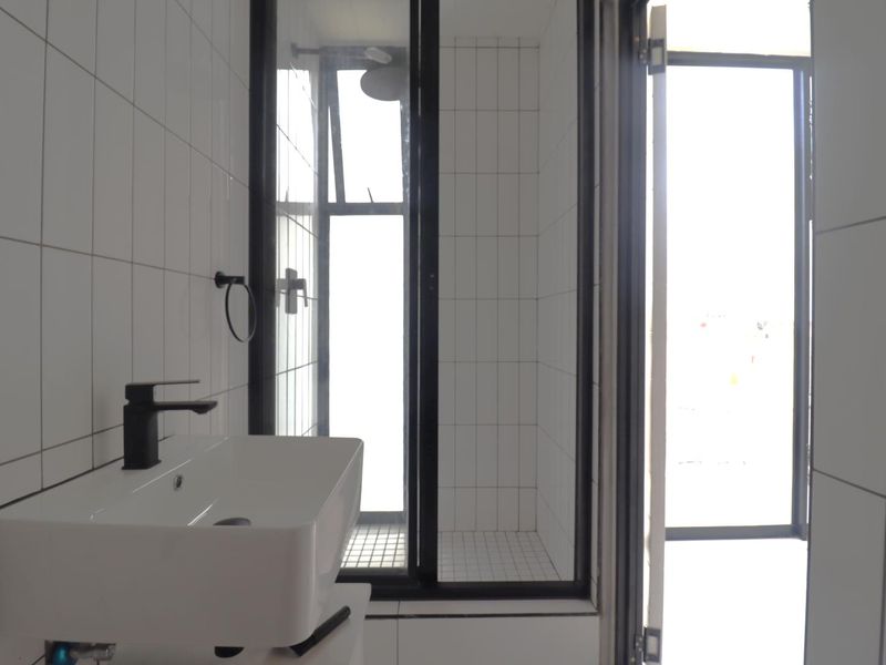 A modern, minimalist bathroom featuring a wall-mounted basin with a black mixer tap and a separate shower enclosure with black framing.