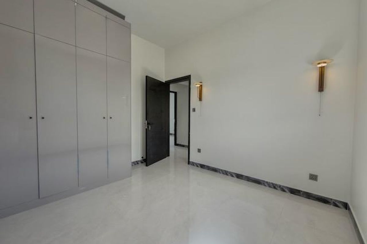 A bright, modern bedroom featuring high-gloss built-in wardrobes, sleek tiled flooring, and contemporary wall sconce lighting.