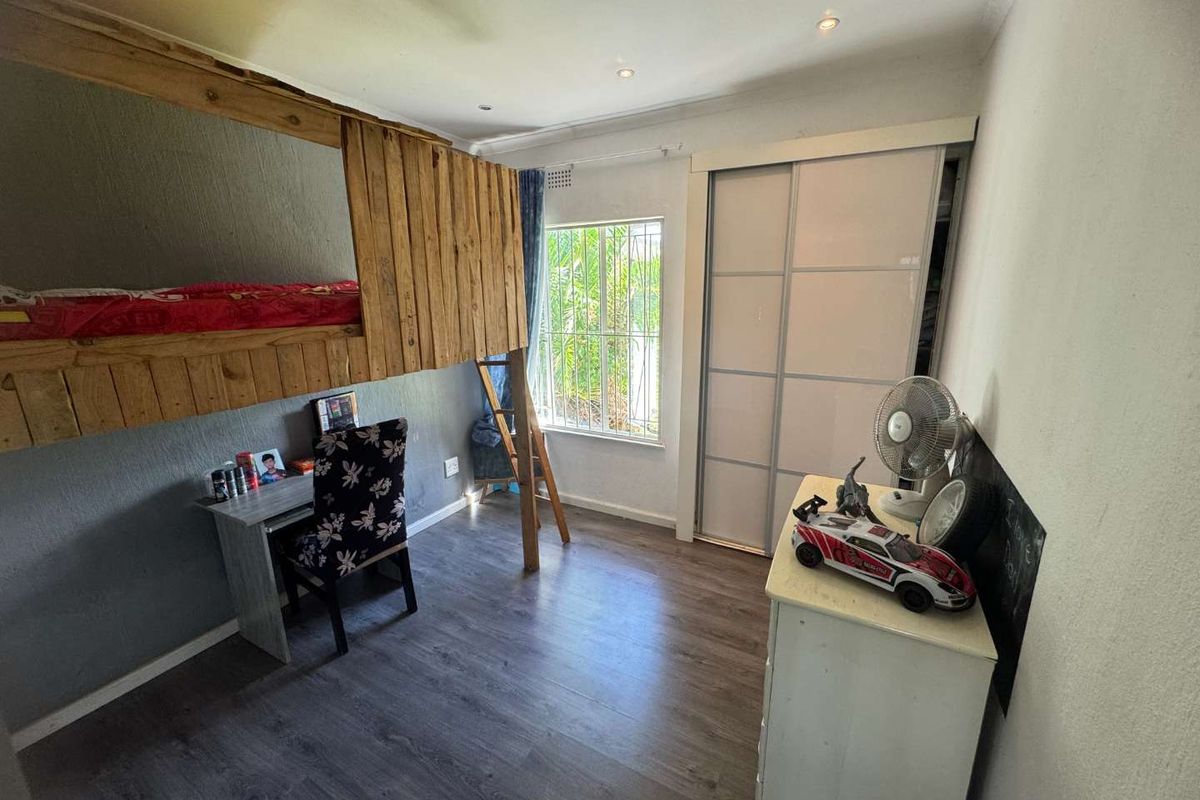 A bedroom featuring wood-look laminate flooring, built-in sliding door cupboards, and a window with security bars.