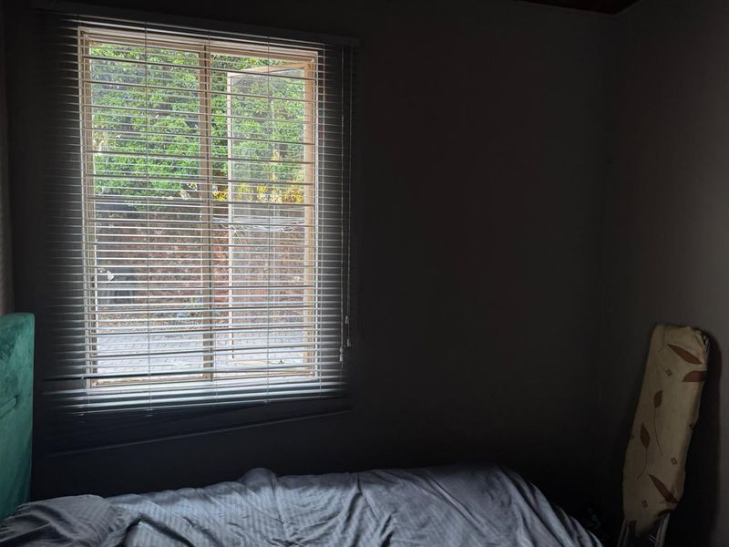 A bedroom featuring a casement window with fitted venetian blinds, providing natural light and a view of the exterior area.