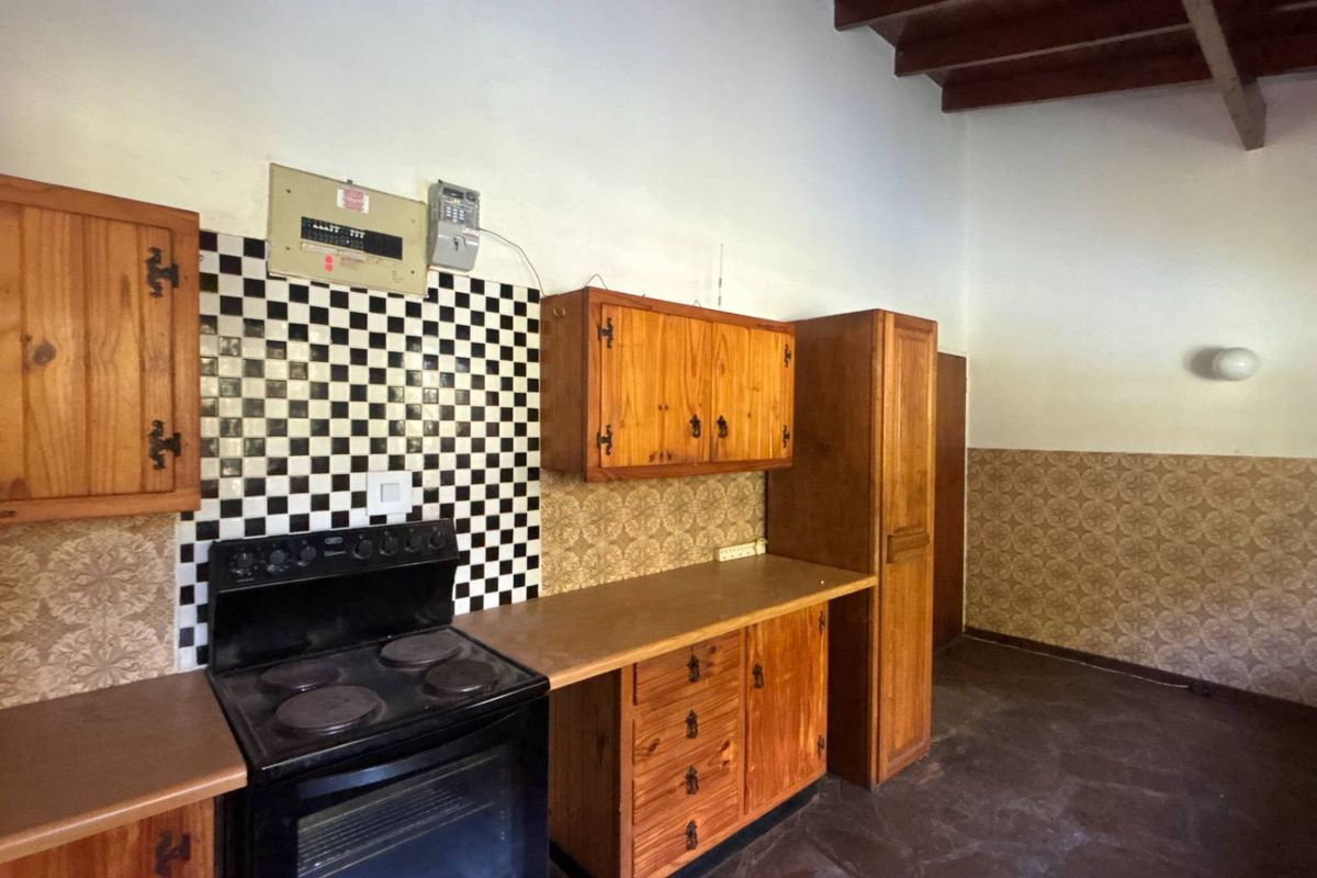 A dated kitchen featuring wooden cabinetry, a checkerboard tile backsplash, an electric stove, and exposed ceiling beams, offering significant potential for modernization.