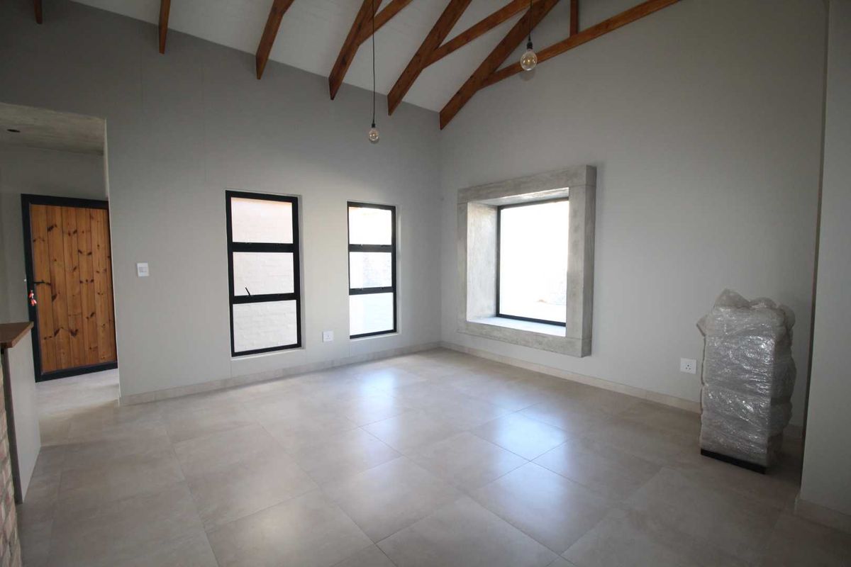 Spacious living area featuring a high vaulted ceiling with exposed timber rafters, modern tiled flooring, and a unique concrete-framed window feature.