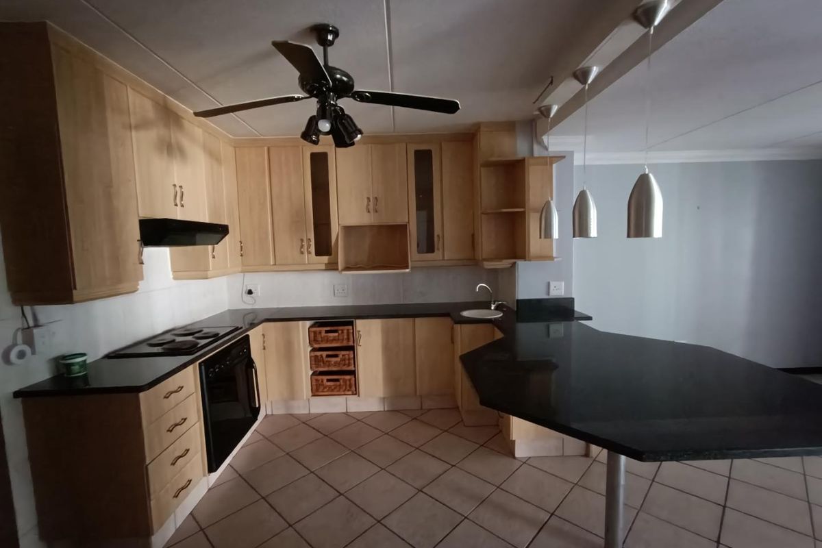 A functional kitchen featuring light wood cabinetry, dark granite countertops, a breakfast bar, built-in oven, and hob with an extractor fan.