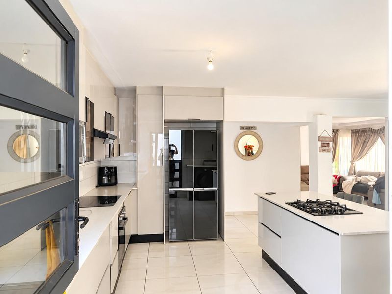 Modern kitchen featuring sleek cabinetry, stone countertops, a central island with a gas cooktop, and high-gloss tiled flooring in an open-plan layout.