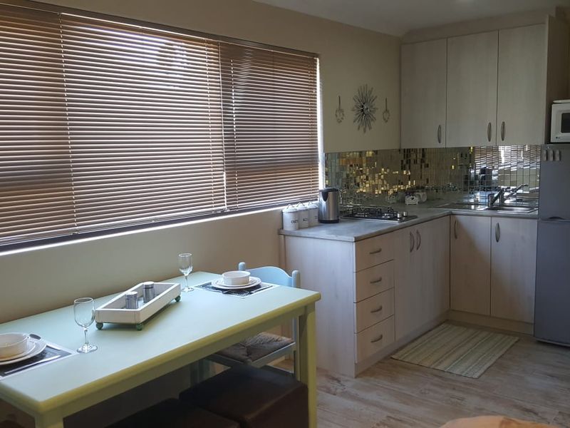 A functional kitchen featuring light-toned cabinetry, laminate countertops, a gas hob, and a decorative tiled backsplash, complemented by large windows with venetian blinds.
