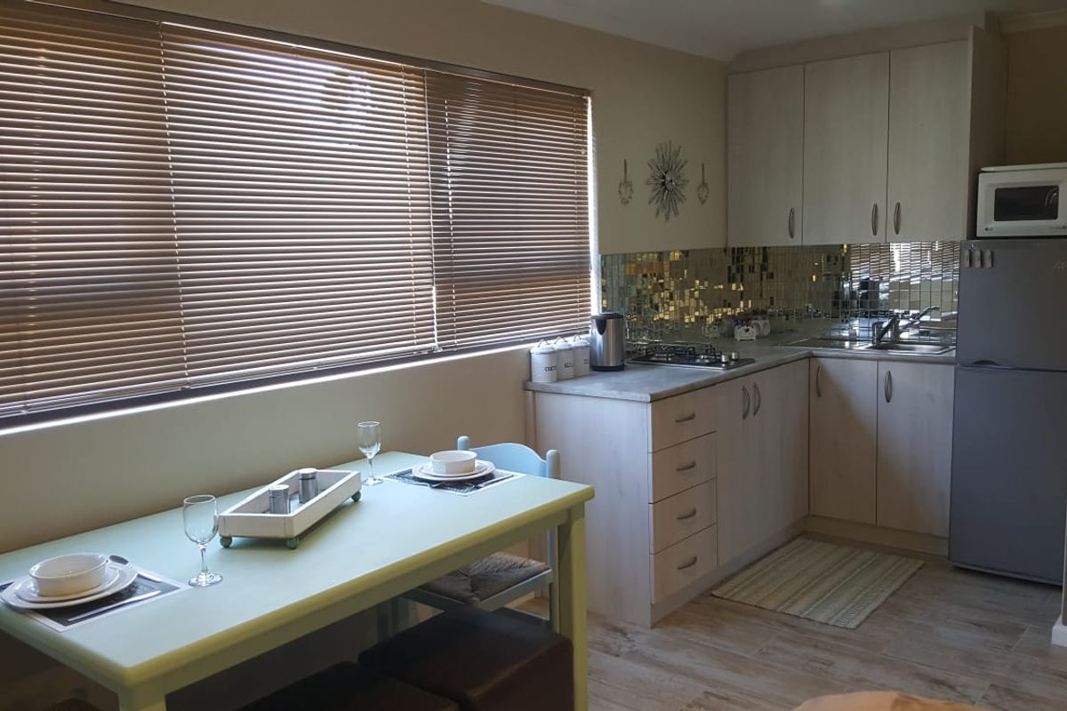 A functional kitchen featuring light-toned cabinetry, laminate countertops, a gas hob, and a decorative tiled backsplash, complemented by large windows with venetian blinds.