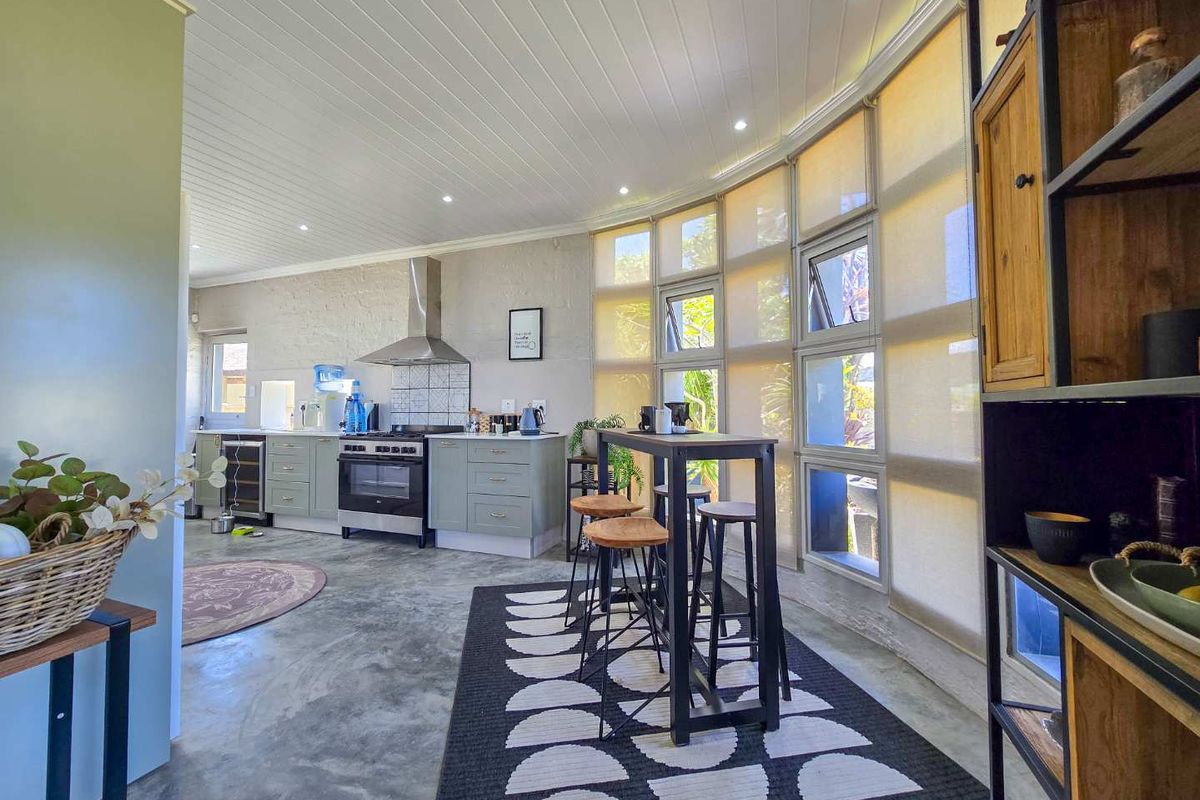 Modern kitchen featuring concrete floors, timber panelled ceilings, stainless steel appliances, and a striking curved glass window wall providing ample natural light.