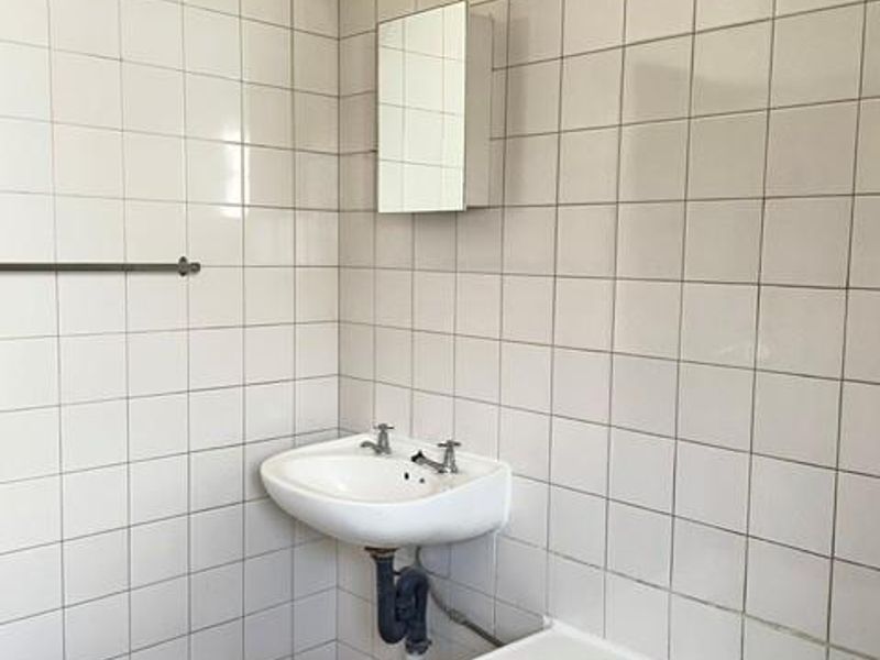 A functional bathroom featuring a wall-mounted basin, bathtub, and tiled finishes, offering a blank canvas for modernization and cosmetic updates.