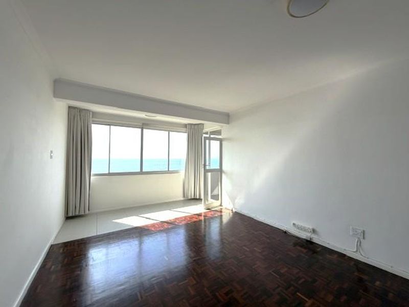 An empty living room featuring dark parquet flooring, large windows with ocean views, and access to a balcony area.