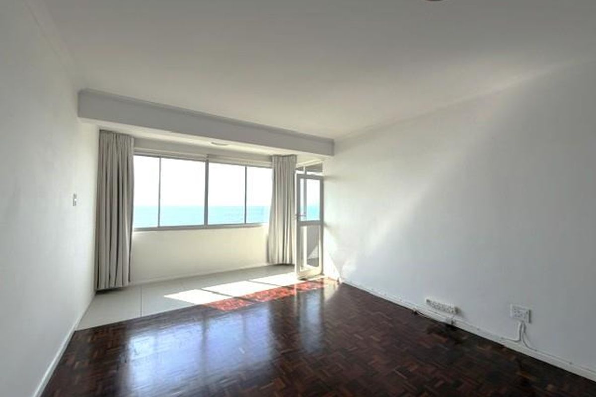 An empty living room featuring dark parquet flooring, large windows with ocean views, and access to a balcony area.