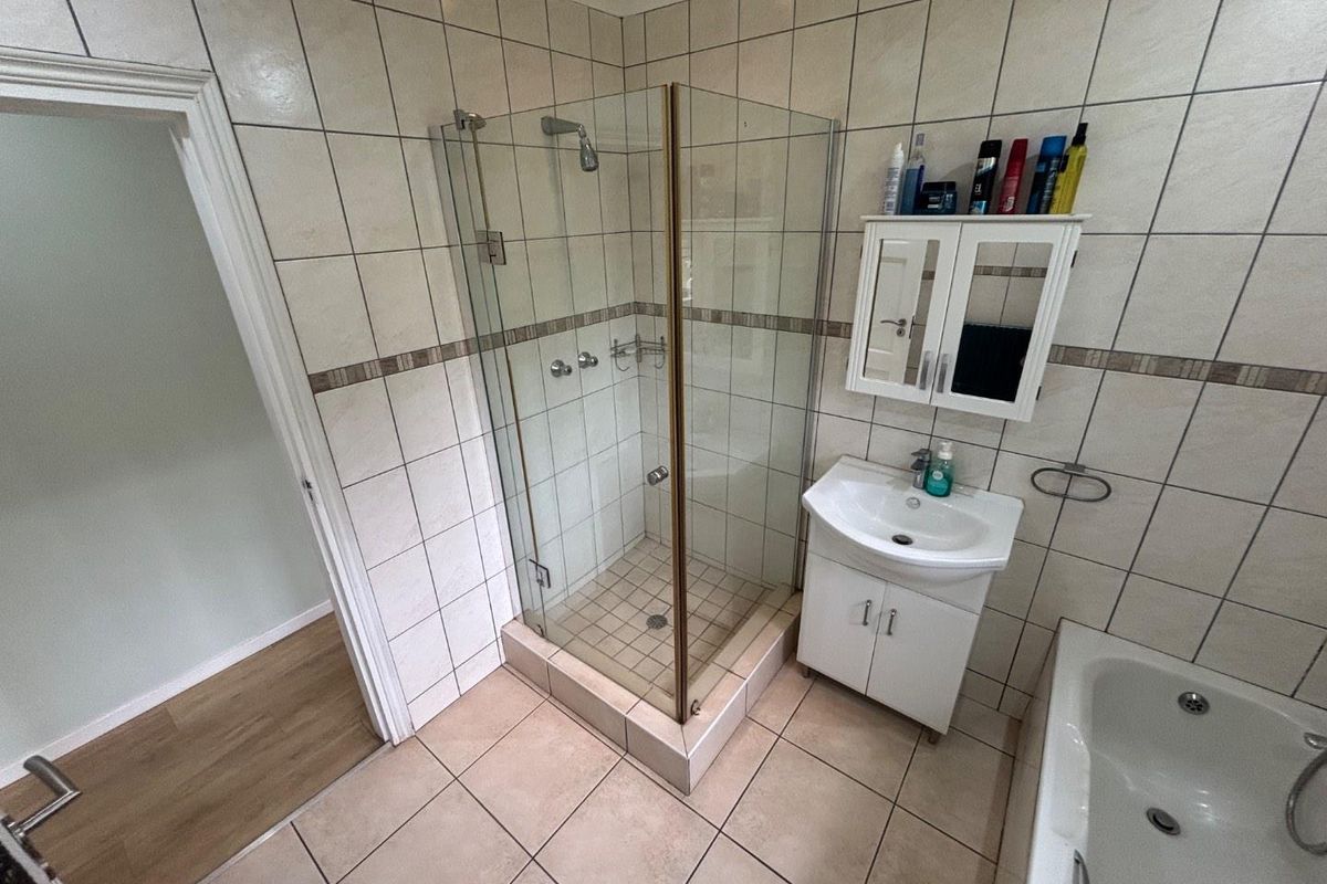 A functional bathroom featuring a glass-enclosed shower, a vanity basin with storage, and a bathtub with tiled walls and flooring.