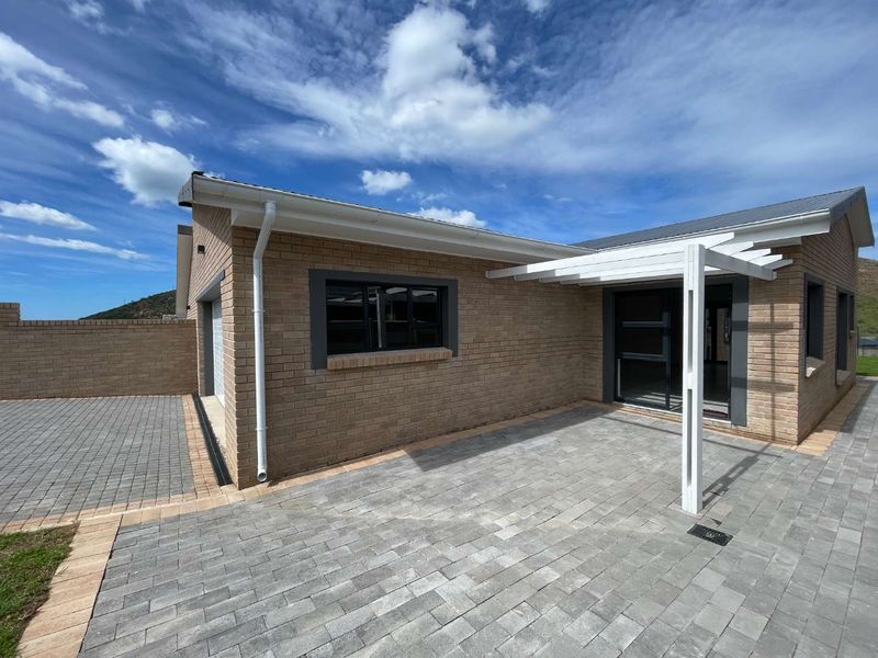 A well-maintained rear exterior view featuring a paved patio area with a pergola, brick facade, and paved driveway access.