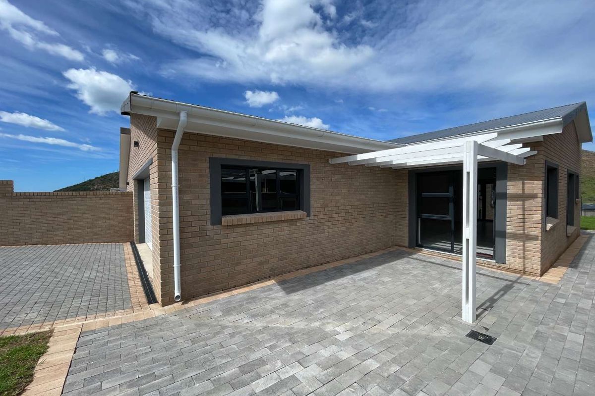 A well-maintained rear exterior view featuring a paved patio area with a pergola, brick facade, and paved driveway access.