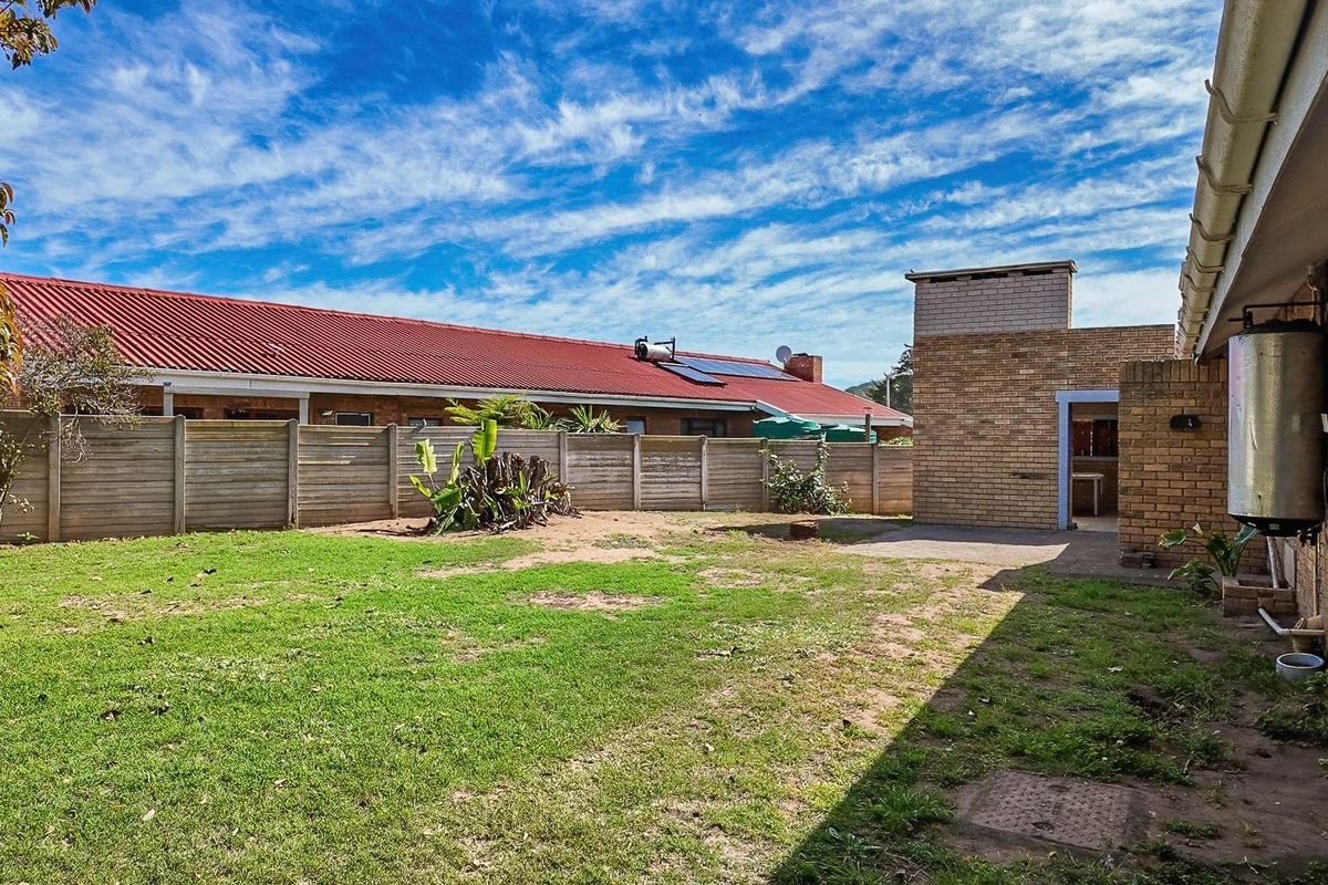 A spacious rear garden featuring a lawn area, brick boundary wall, and a brick-built utility structure attached to the main house.