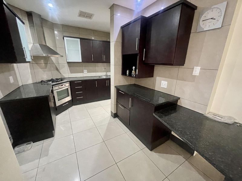 Modern kitchen featuring dark wood cabinetry, granite countertops, stainless steel appliances, and neutral tiled flooring throughout.