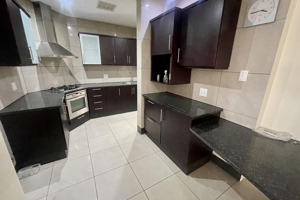 Modern kitchen featuring dark wood cabinetry, granite countertops, stainless steel appliances, and neutral tiled flooring throughout.
