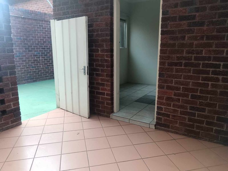 A rear exterior view of a townhouse featuring a brick facade, tiled patio area, and an open doorway leading into the interior space.