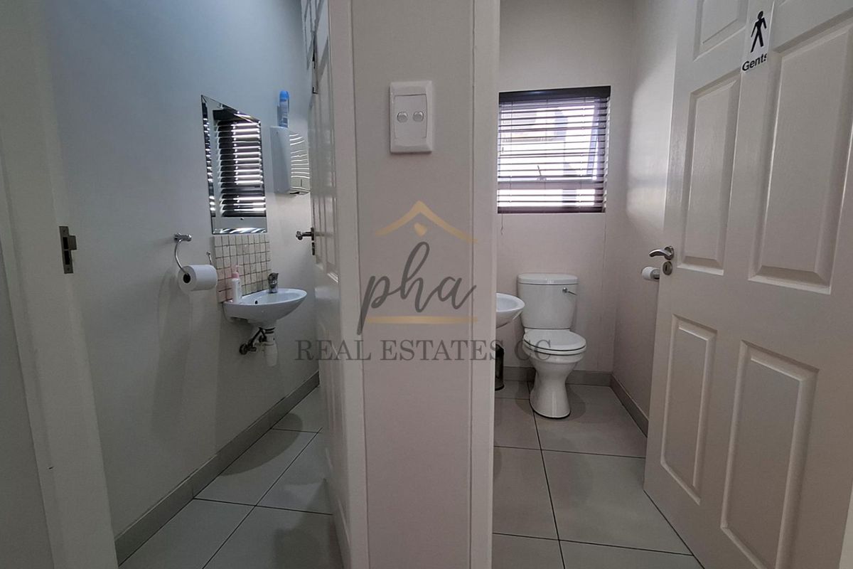 A clean and functional office restroom facility featuring tiled flooring, wall-mounted basins, and a private toilet cubicle with a window.