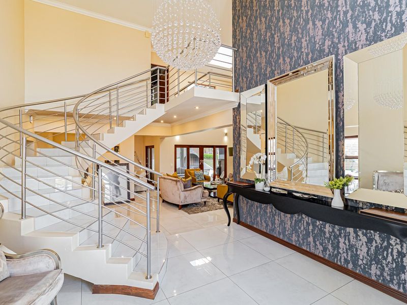 Grand entrance hall featuring a striking curved staircase with stainless steel balustrades, polished porcelain flooring, and a dramatic feature wall with a crystal chandelier.
